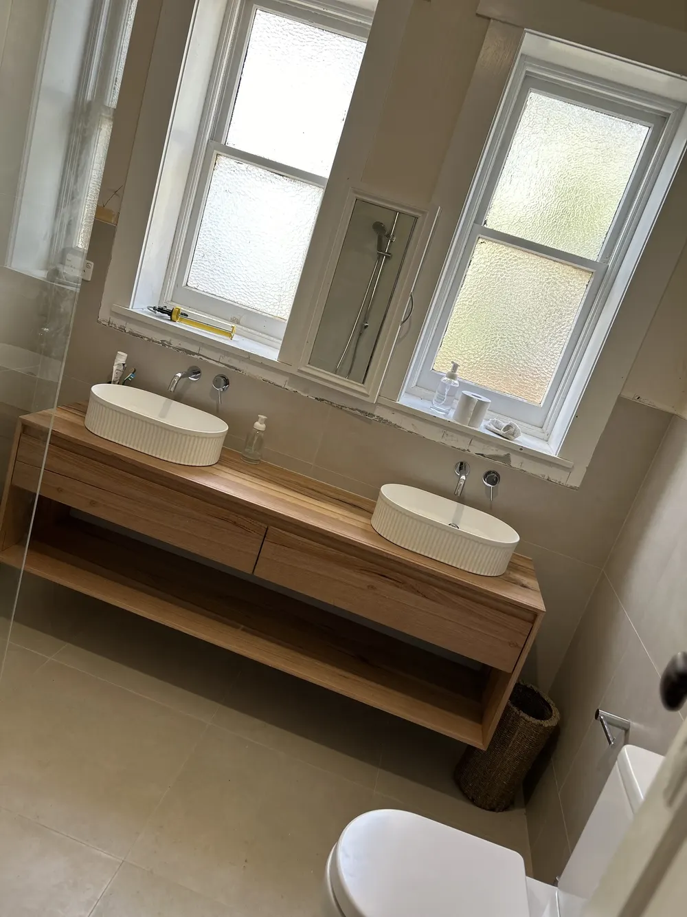 Double-basin timber bathroom vanity beneath frosted windows