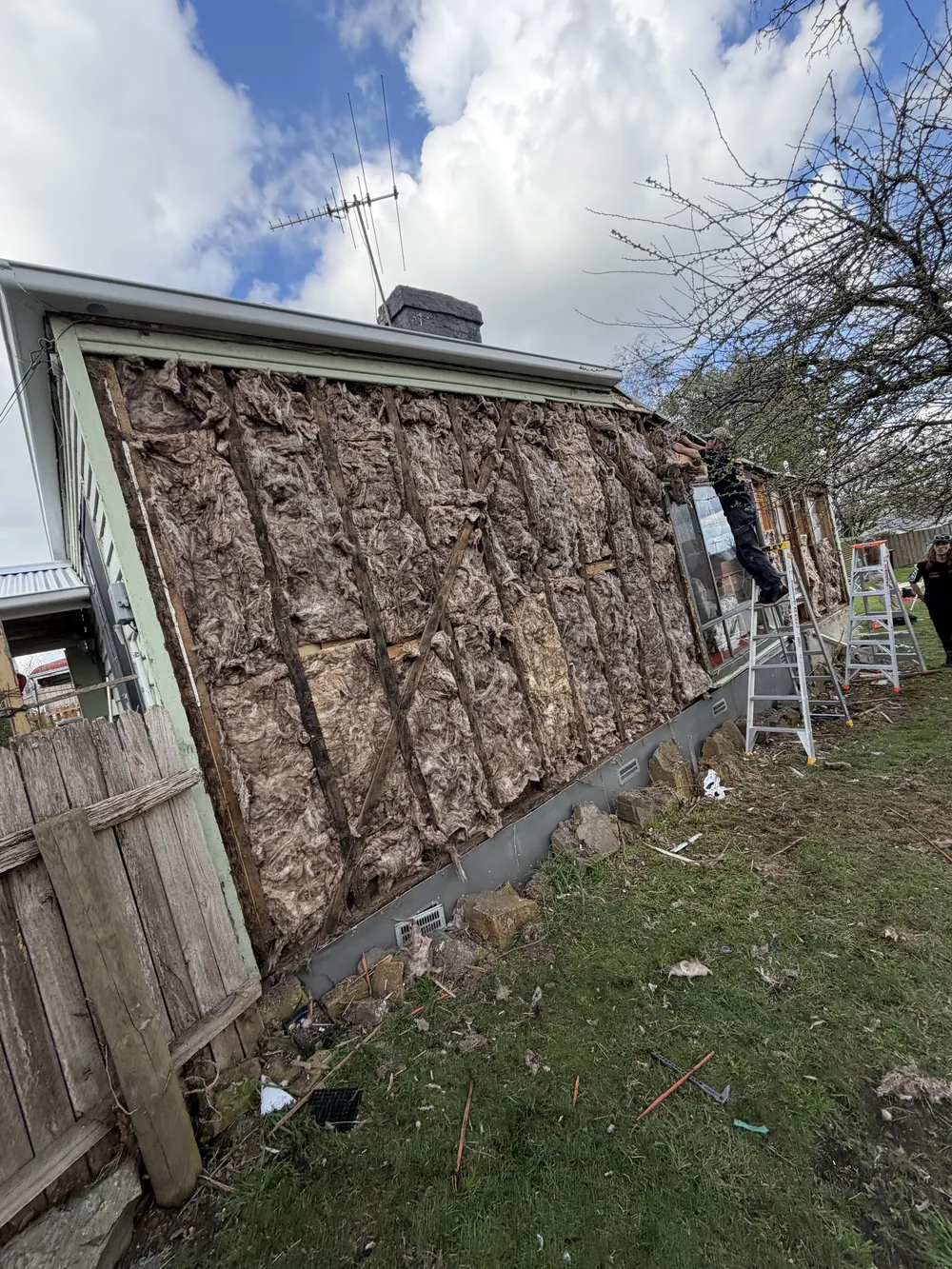 Exterior wall with cladding removed and ladders beside the work area