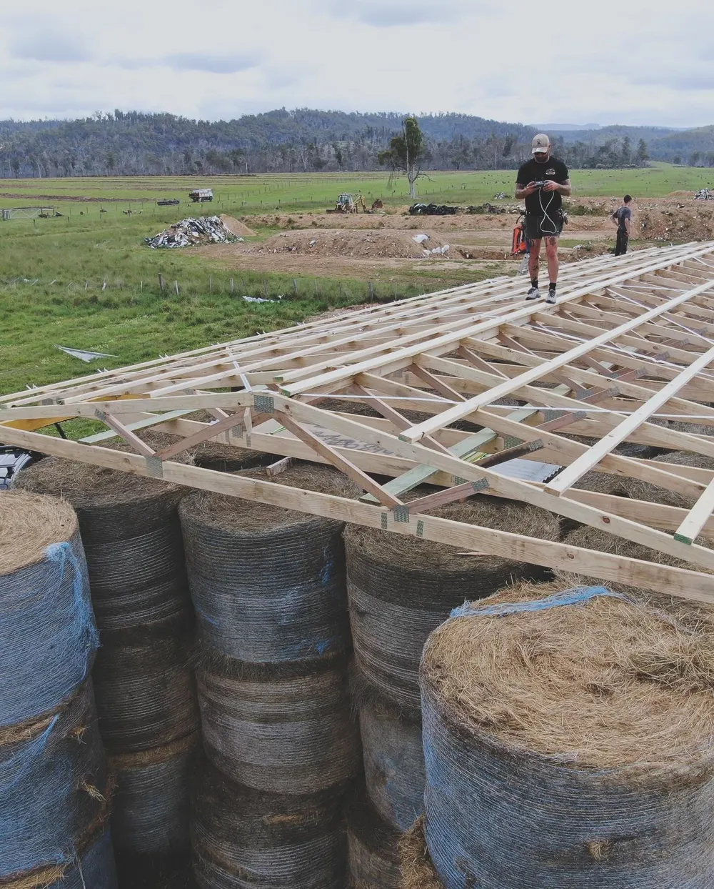 Timber framing raised over round hay bales on a rural building site