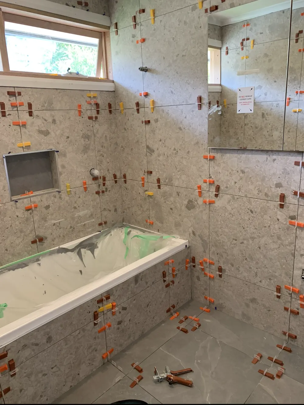 Bathroom wall and floor tiles with levelling clips around a protected bath