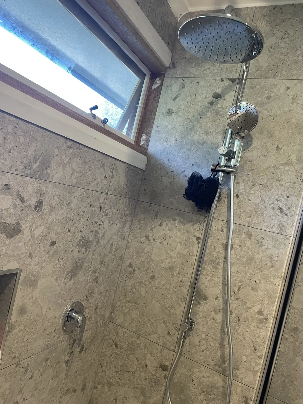 Black shower head and handheld shower against stone-look wall tiles