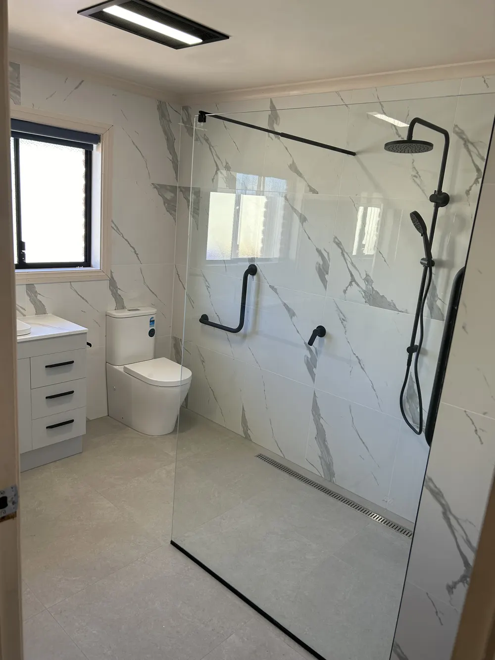 Bathroom with marble-pattern wall panels, glass shower screen and black shower fittings